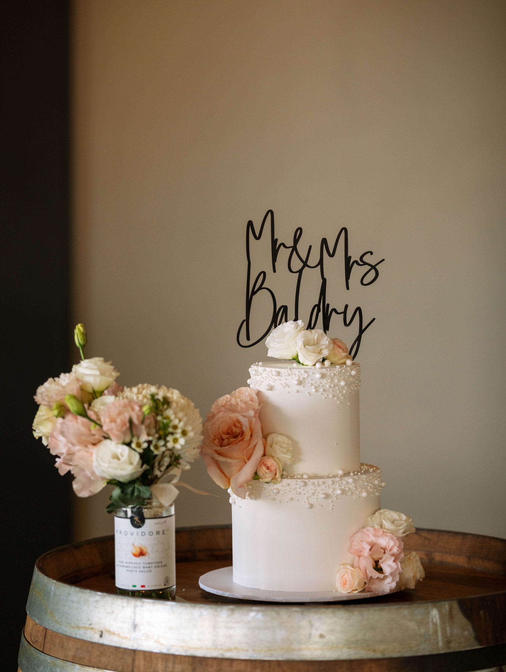 two tier wedding cake with black personalised topper, fresh pink and peach flowers and sugar pearls