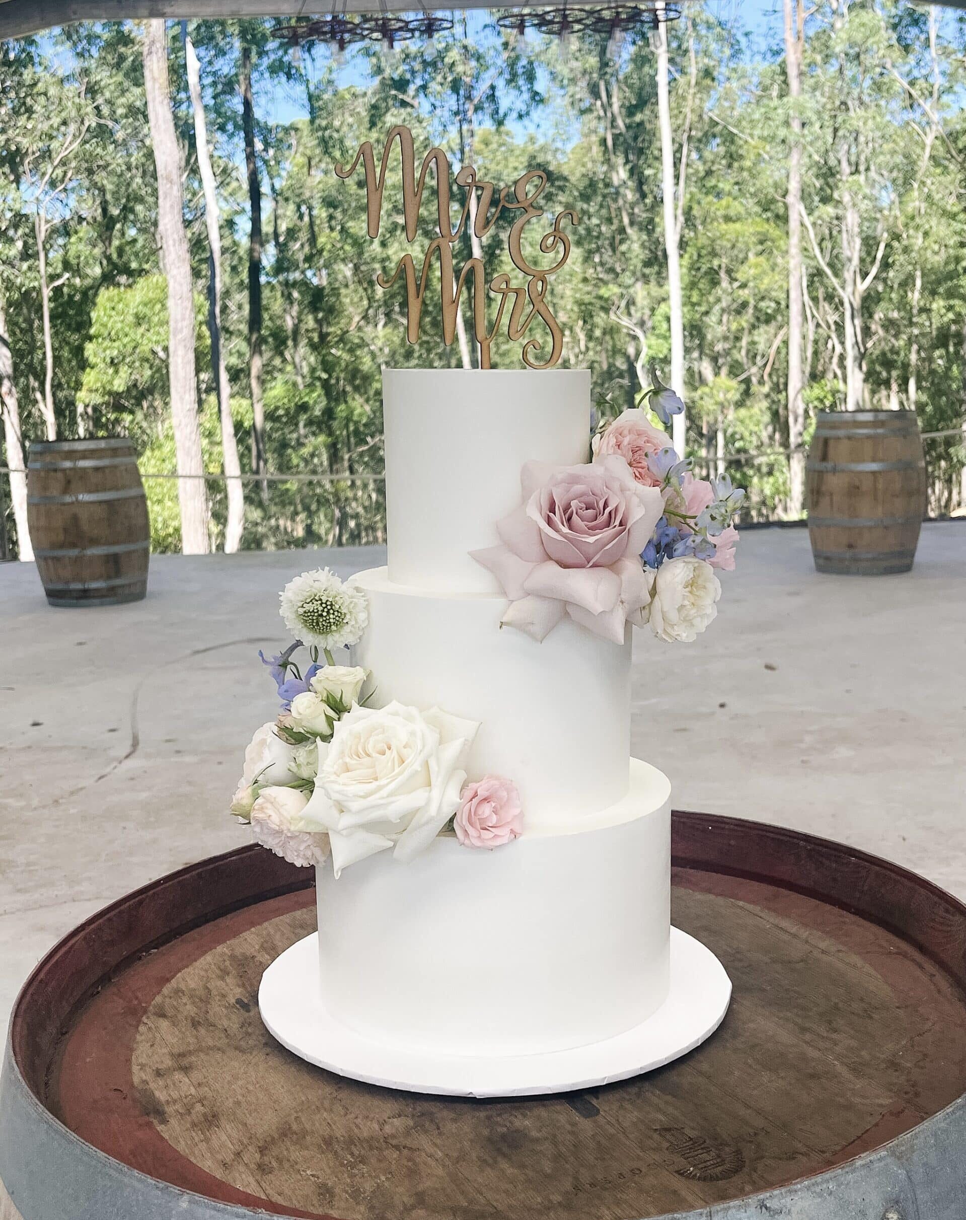 3 tier white ganache cake decorated with fresh flowers in pinks, white and blues